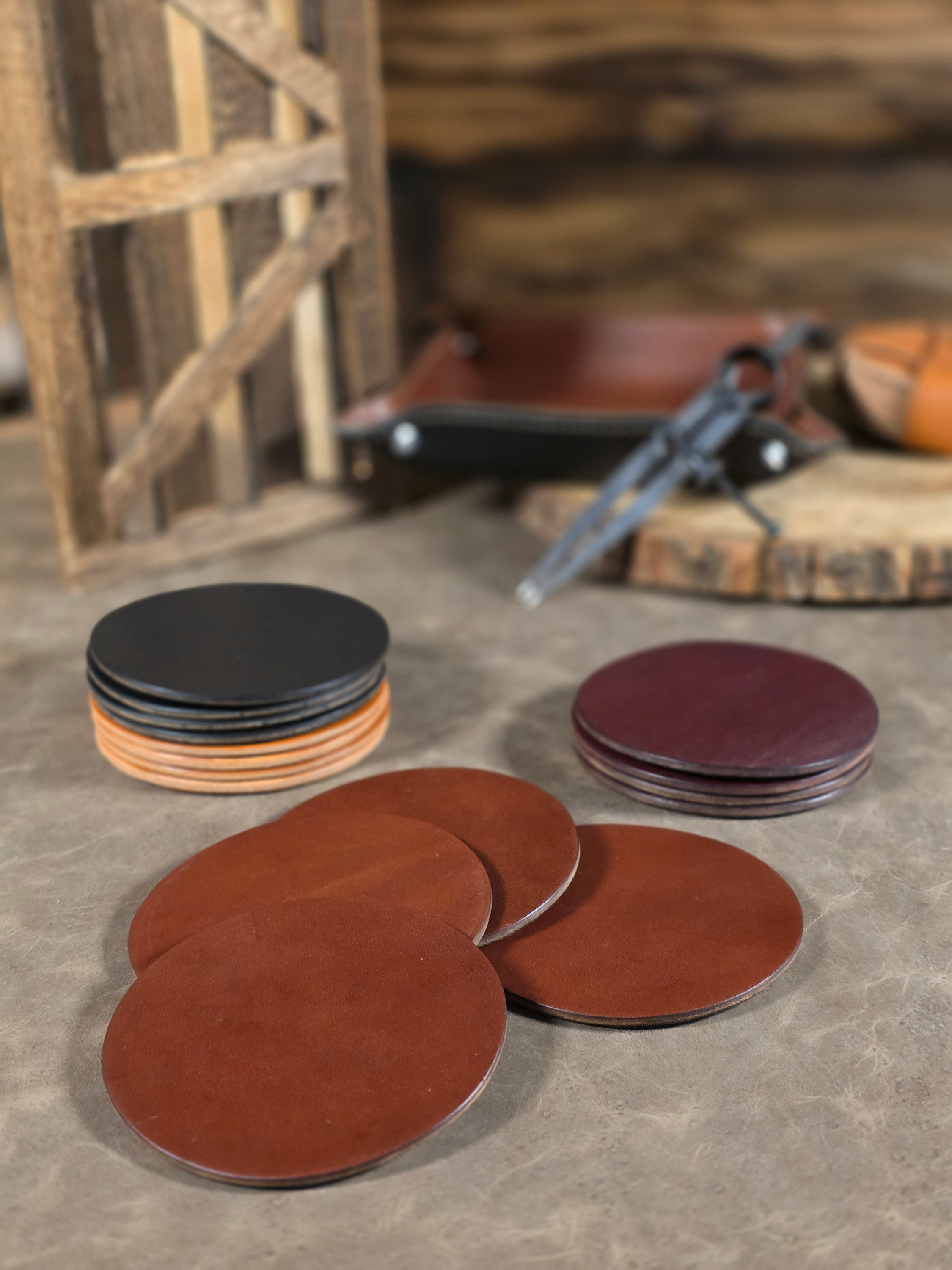 Stacks of round leather coasters in black, brown, and red on a stone surface with a rustic background.