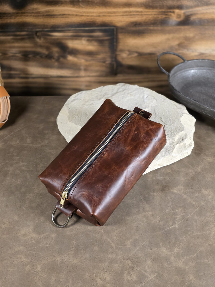 Antique copper colored leather pouch with a zipper on a stone surface with a wooden background