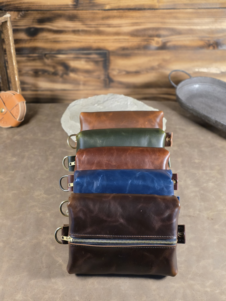 Set of leather dopp kit pouches arranged in a line in various colors on a wooden surface