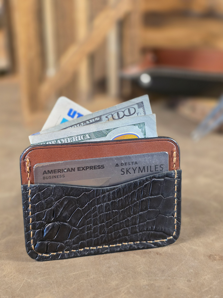 Black alligator leather wallet with cards and money on a wooden surface