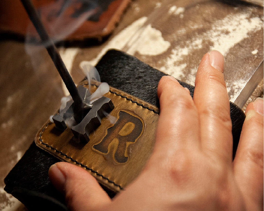 Closeup image of the letter M being hot-branded into a leather koozie