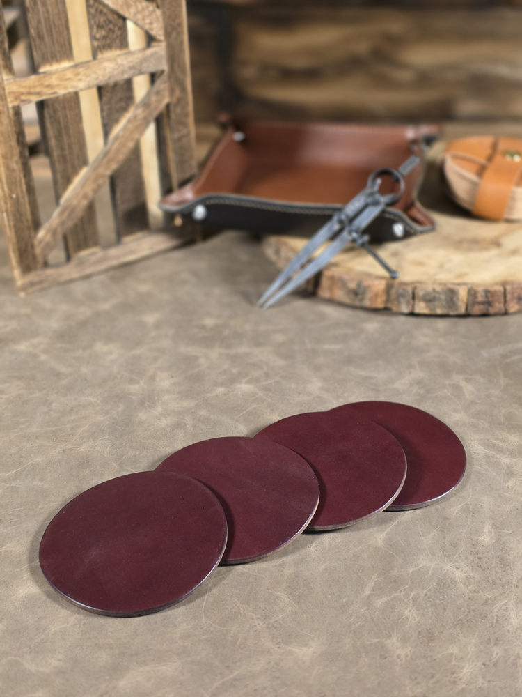 Set of oxblood leather coasters on a concrete surface with tools and a wooden board in the background.