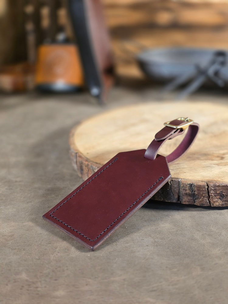 Oxblood leather luggage tag on a wooden surface with a blurred background