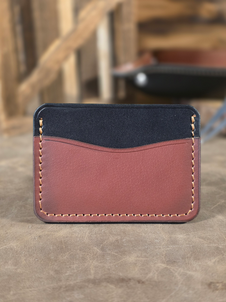 Two-tone leather wallet with black top section and oxblood colored bottom section on a wooden surface.