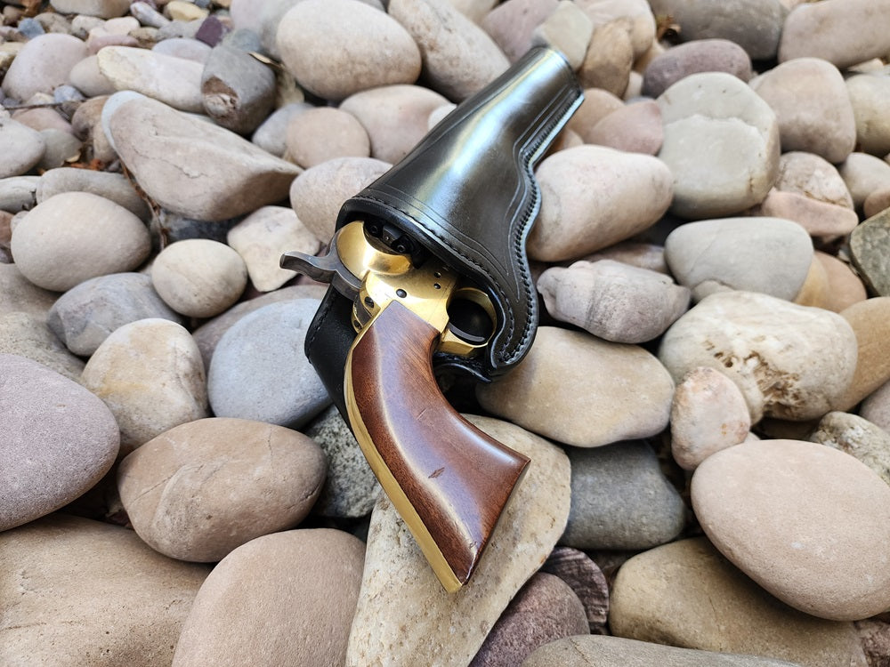 View of wild bills hickoks holster from the mouth of the holster. A 1873 colt Peacemaker is holstered and the holster is sitting on a bed of rocks.