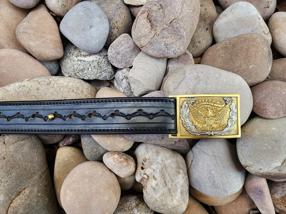 Black leather replica of Wild Bill Hickok's belt with a gold and silver cavalry officer buckle. The belt sits on a bed of pale stones.