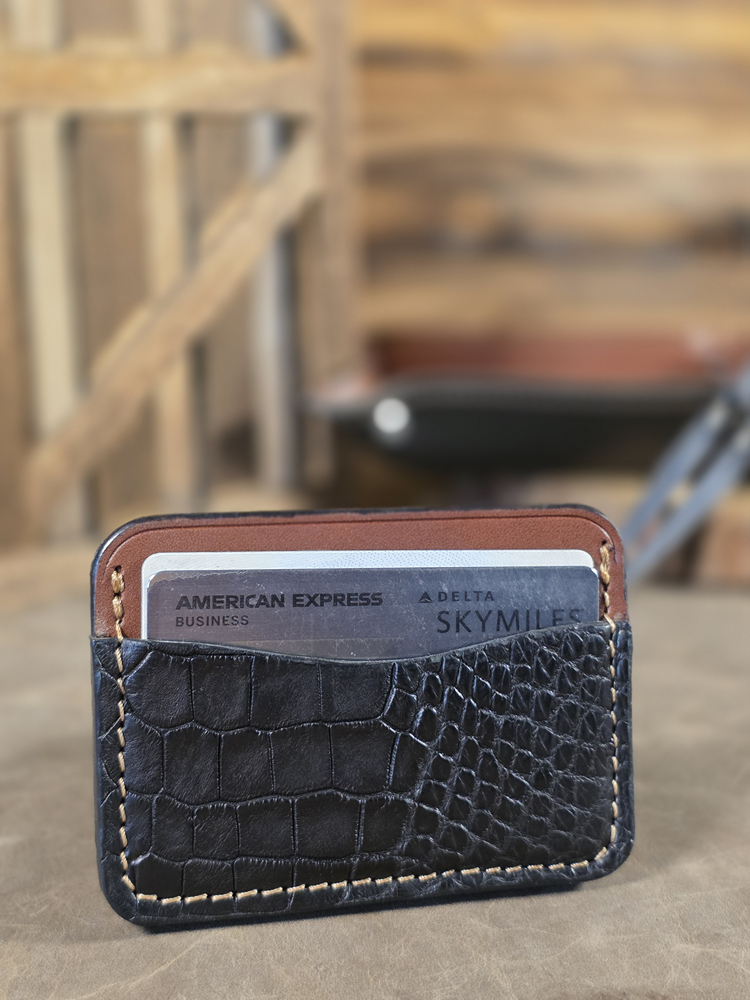 Black alligator card wallet with American Express and Delta cards on a wooden surface.