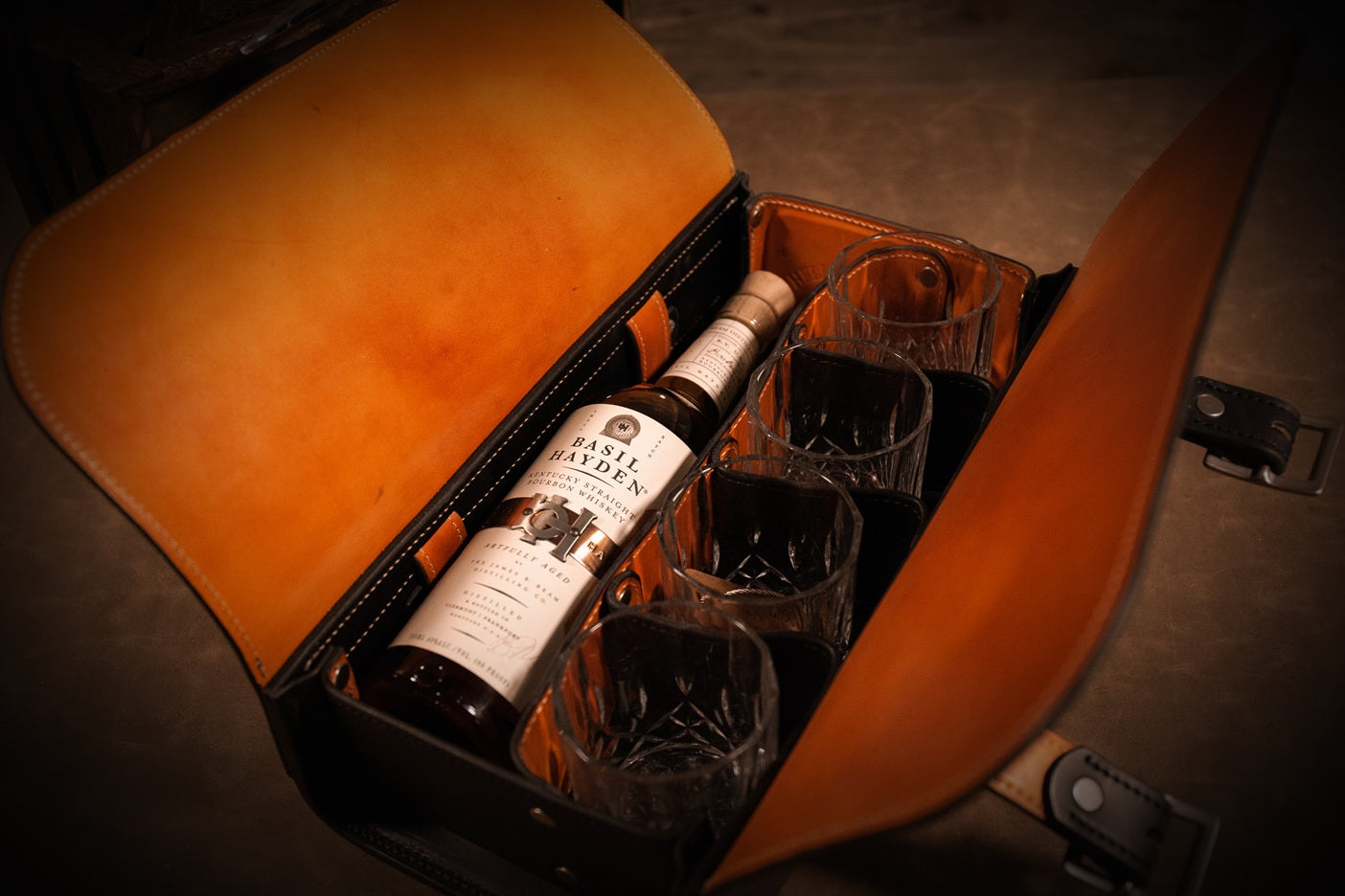 Interior view of the Syndicate Bourbon Bag, showing a bottle of Basil Hayden and four securely separated rocks glasses. The interior leather is tan.