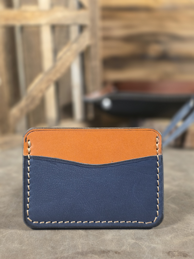 Two-tone navy and tan leather cardholder on a wooden surface with blurred background
