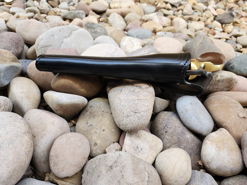 View of a black leather replica of Wild Bill hickok's holster from the side, a 1873 Colt Peacemaker is holstered. The holster sits on a bed of rocks.
