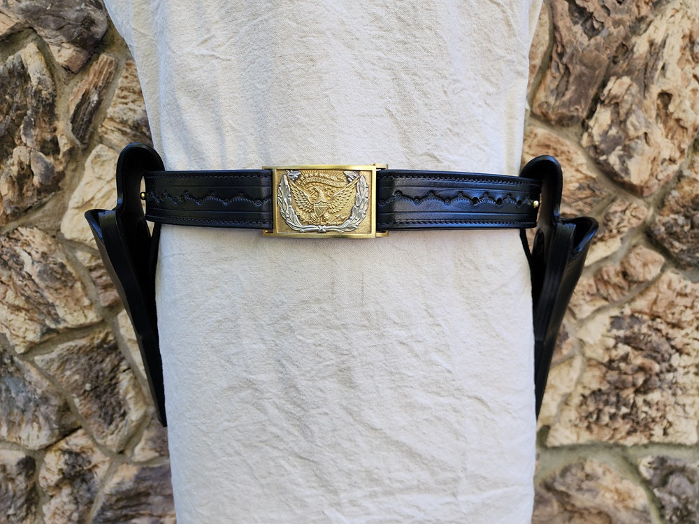 Black tooled leather replica of Wild Bill Hickok's gun rig placed on a white mannequin. The piece features two holsters of matching style and color, additionaly it features a gold and silver classic cavalry buckle.