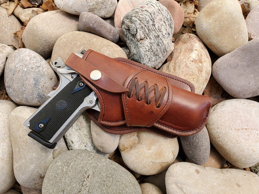 Western style 1911 holster in full grain leather and a laced collar sitting on smooth river rock.