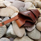 A full grain leather holster sitting against a river rock background. The interior of the holster is visible to show the smooth high quality leather lining.