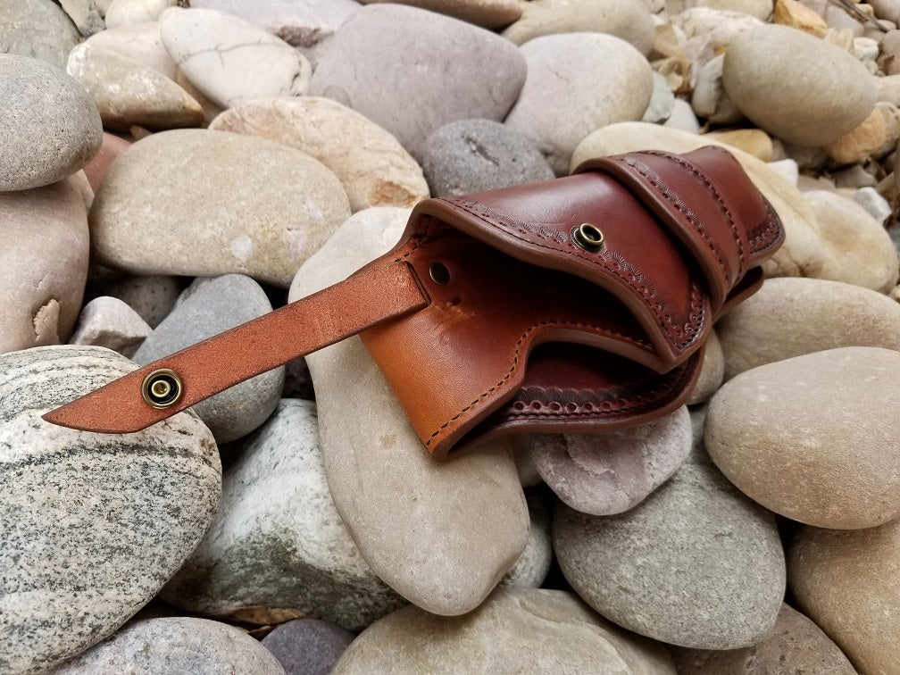 A full grain leather holster sitting against a river rock background. The interior of the holster is visible to show the smooth high quality leather lining.