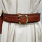 Sturdy brown leather western cowboy gunbelt with a shiny brass buckle wrapped around a mannequin draped in white canvas