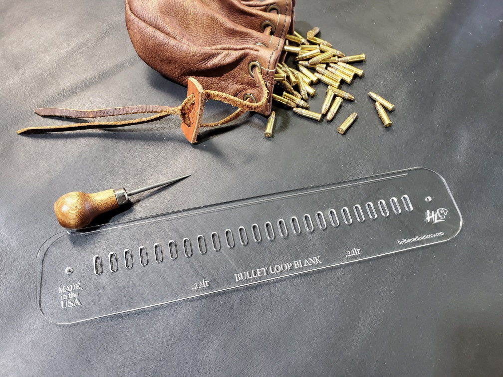 An acrylic bullet loop pattern used in leathercraft to mark the spacing between bullet loops on a western gun belt sits next to a leather drawstring bag full of .22 bullets.