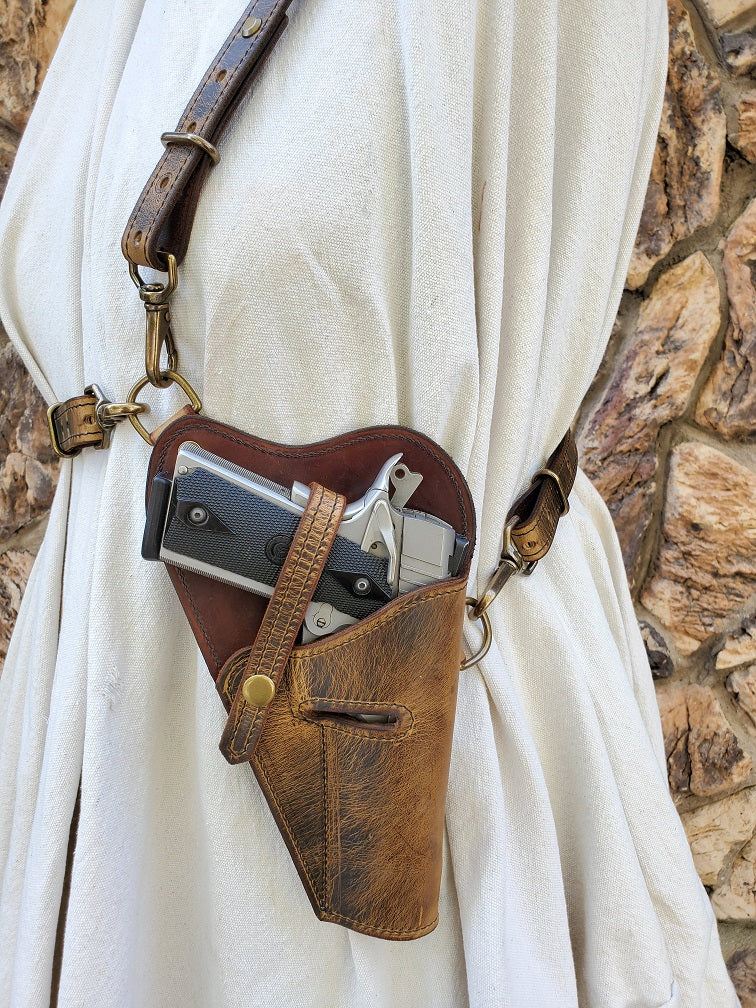 Vintage shoulder holster fitted with solid natural brass hardware and a silver M1911 holstered via retention straps.