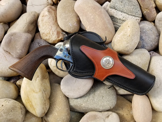 Black and brown two-toned leather western holster with compass concho laying on smooth river rocks