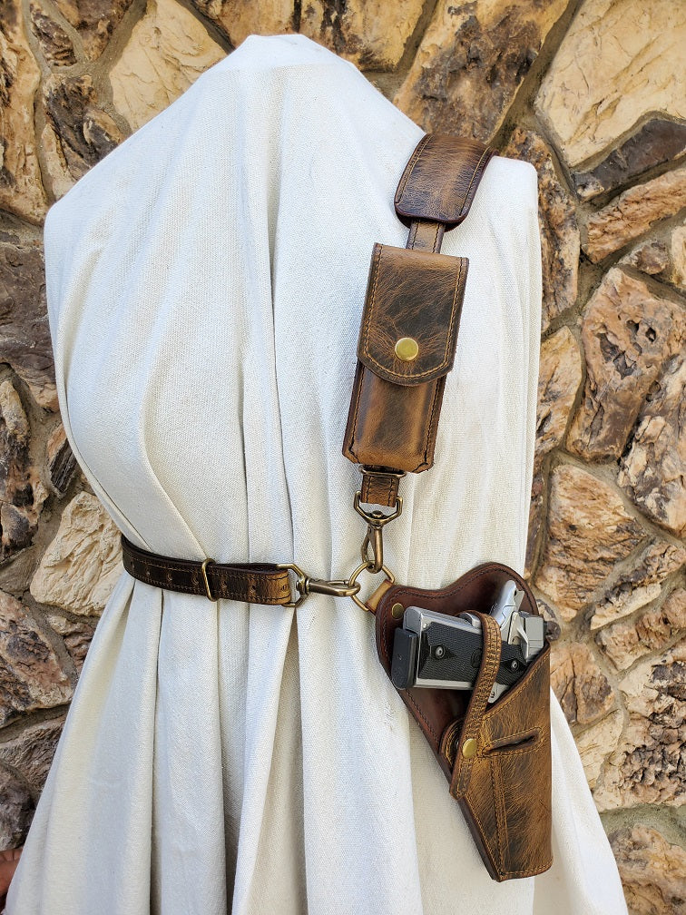 Distressed brown leather shoulder holster and mag pouch for M1911 sidearm. Featuring solid brass hardware the piece is mounted into a mannequin with a jagged rocky background.