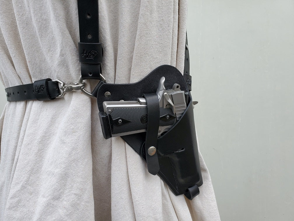 Black shoulder holster featuring solid brass hardware with nickel matte finishing, a silver M1911 holstered using retention straps.