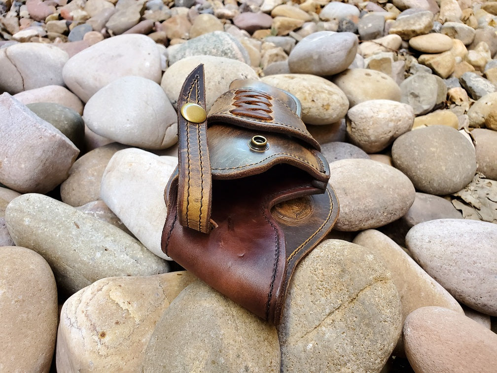 View of a vintage brown ghostwood holster from the mouth end without firearm insert. The piece is done with criss cross lacing and is sitting on a bed of river rocks.