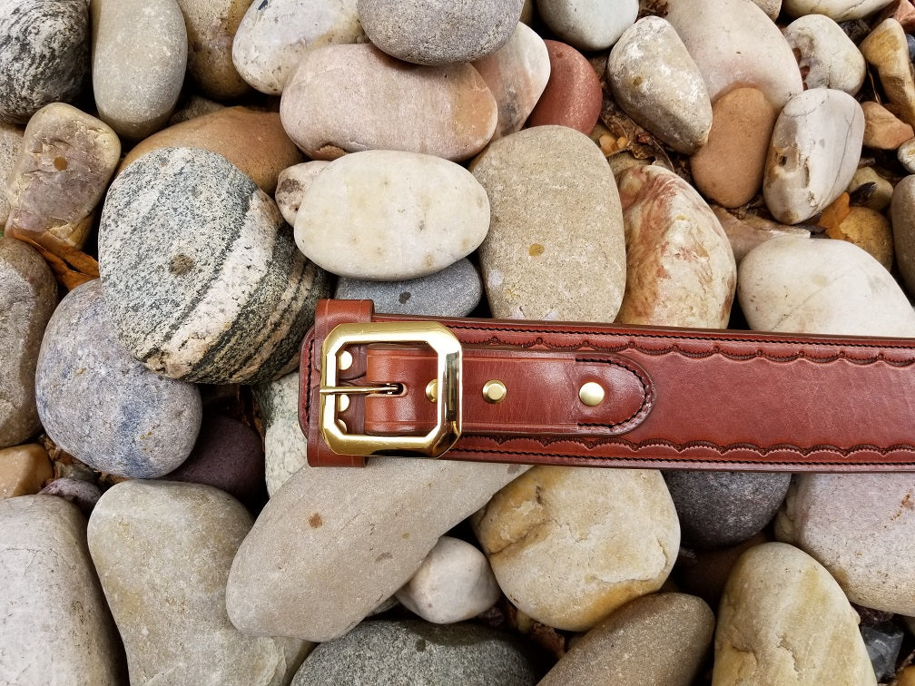 Buckle of the the widow rock belt. The piece is made of brown leather and solid brass hardware with scallop pattern tooling along the borders.