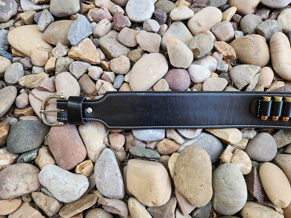 View focusing on the buckle end of the belt, the buckle is solid brass nickel hardware, the belt is stitched with white thread and the belt is layed out on pale river rocks.