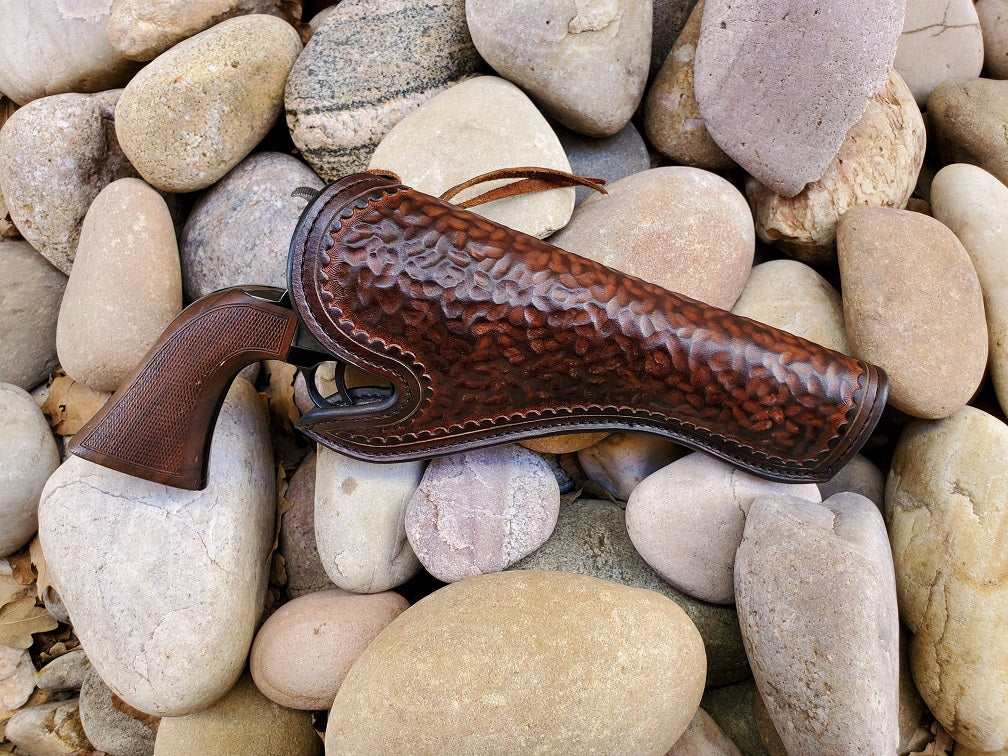 Dark brown California style leather holster with a hammered texture sits on a background of river rocks.