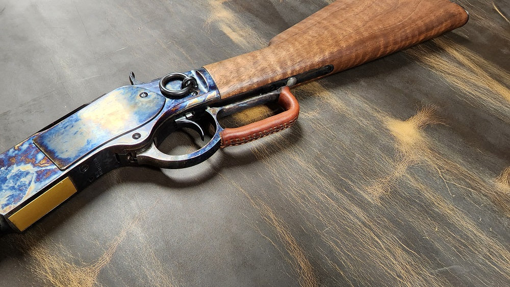 Winchester lever action rifle with a brown leather wrap on the lever of the gun, the gun sits on a distressed leather background.