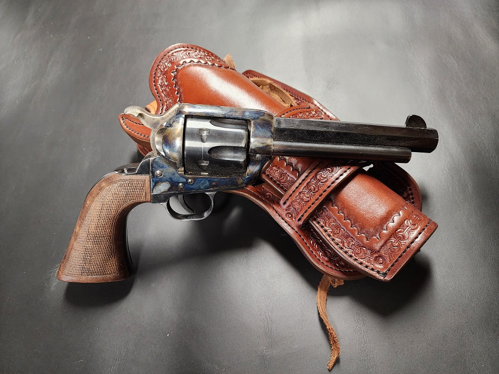Revolver sitting on top of the brown leather tooled double Mexican loop collared holster, they are both sitting on a bed of black leather.