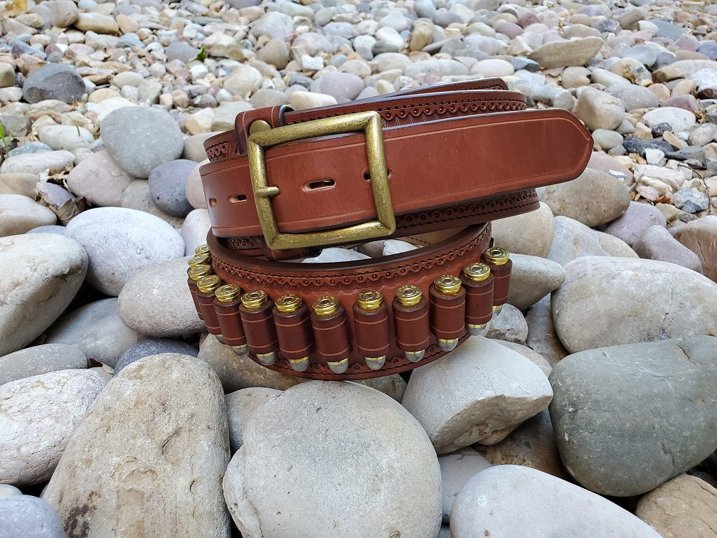 Closeup of a loaded western gun belt with fancy border tooling and antique brass center bar buckle.