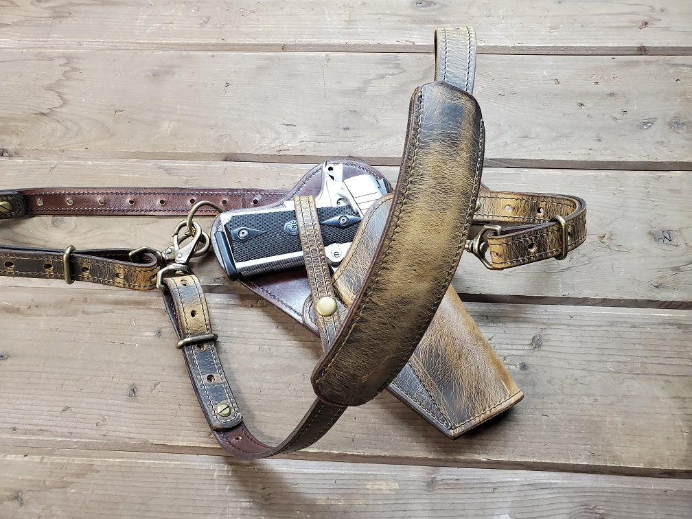 Distressed brown shoulder holster using solid brass hardware, holstering a silver M1911 using retention straps.