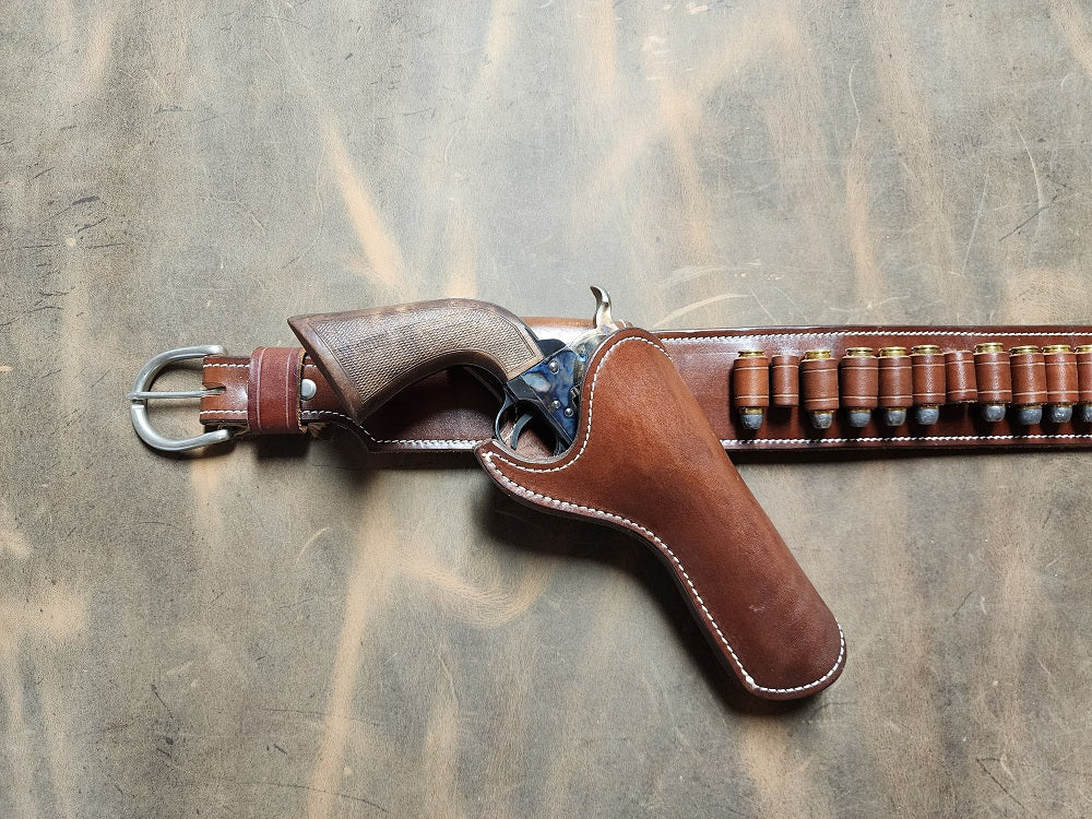 View of the left end of the holster layed out on ghostwood leather, a holster with revolver sits next to the buckle, and just to the right lays the set of bullet loops.