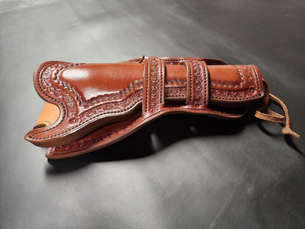 Brown leather intricately tooled leather holster with double Mexican loop collar, the holster is on a black leather background.