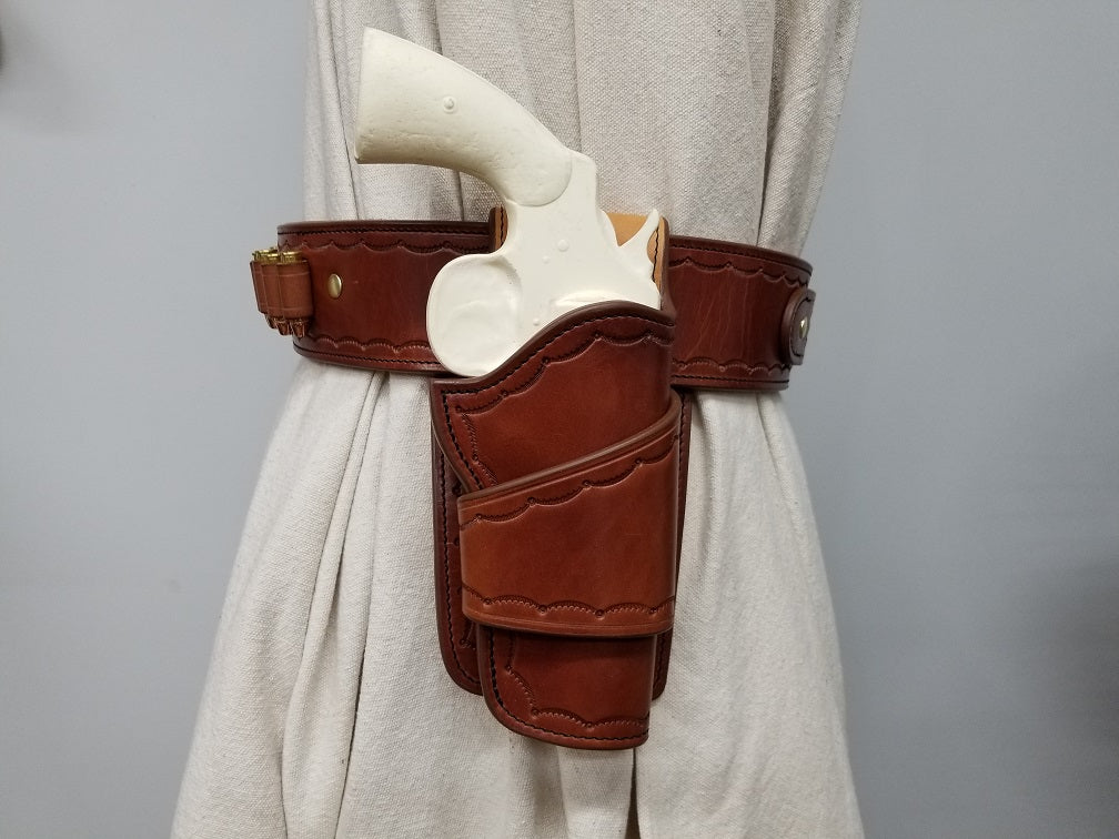 Side view of widow rock gun rig featuring the holster and bullet loops. The rig is made of brown leather with solid brass hardware and it tooled in a scallop pattern along the borders.