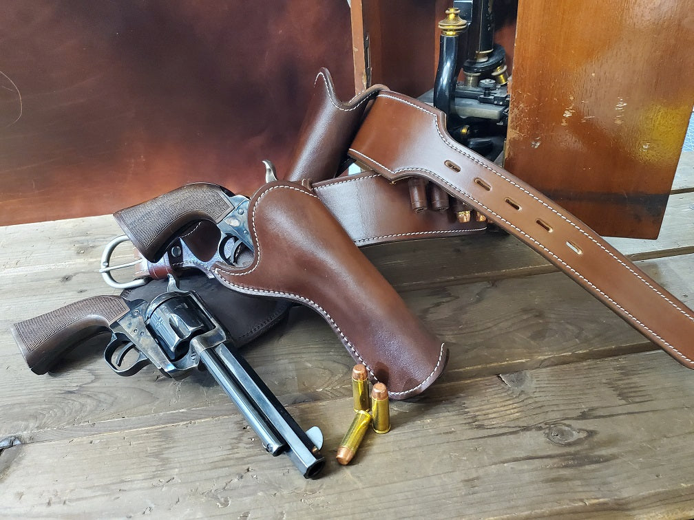 Brown leather Josh Faraday replica gun rig, The piece rests against a box with a old western microscope sitting on wooden slats, next to the gun rig sits a holster and revolver, between the holster and revolver sits three bullets.