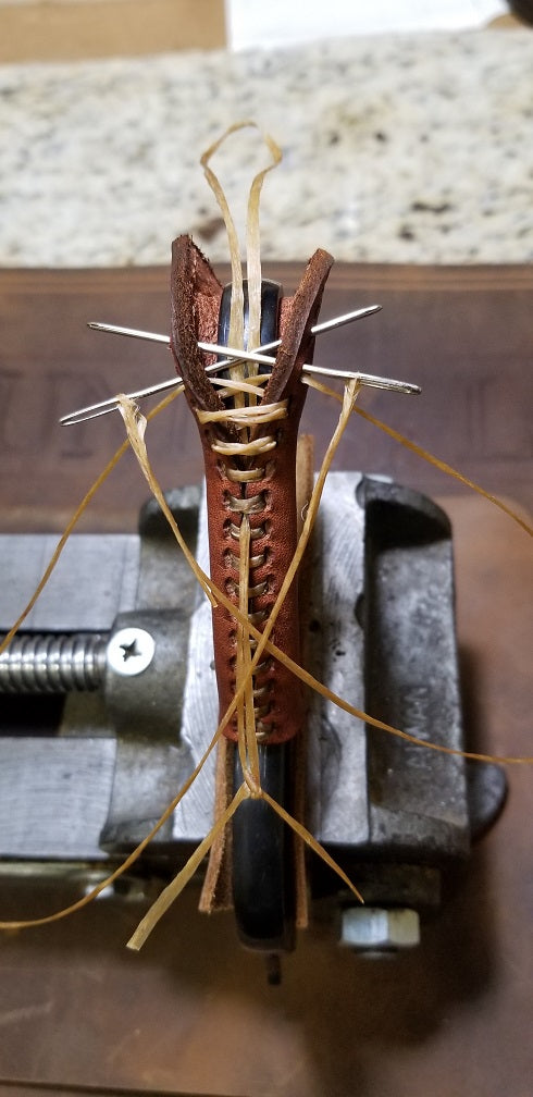 Brown leather wrap being attached to a lever with sinew using needles. The lever is being held in a vice.