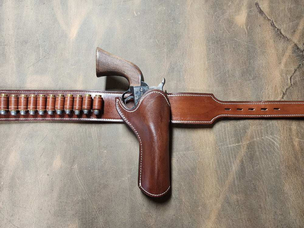 View of the billet end of the gun rig, just to the left of the billet end is the second holster with revolver. Bullet loops lay in the center. The piece lays flat on a bed of ghost wood leather.