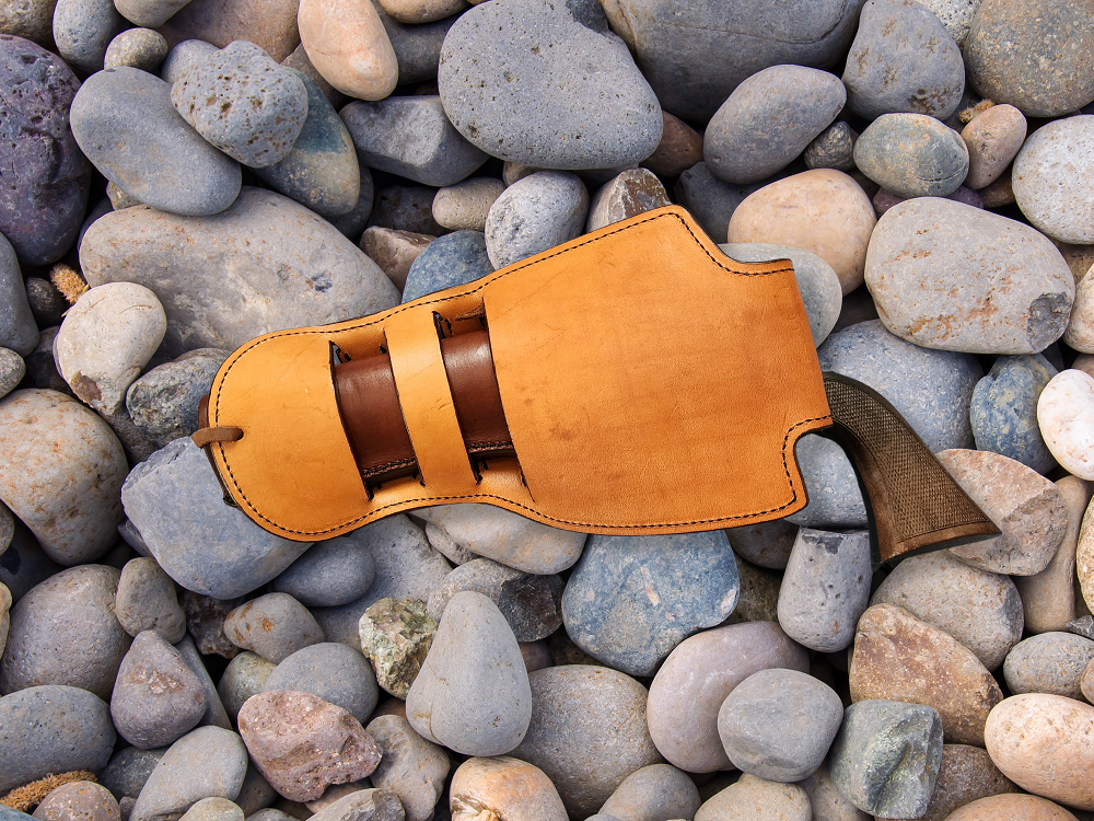 View of the backside of the holster, the leather on the interior and backside of the holster is russet, the grip of the revolver is visible coming out of the holster. The holster is laying on a bed of rocks.