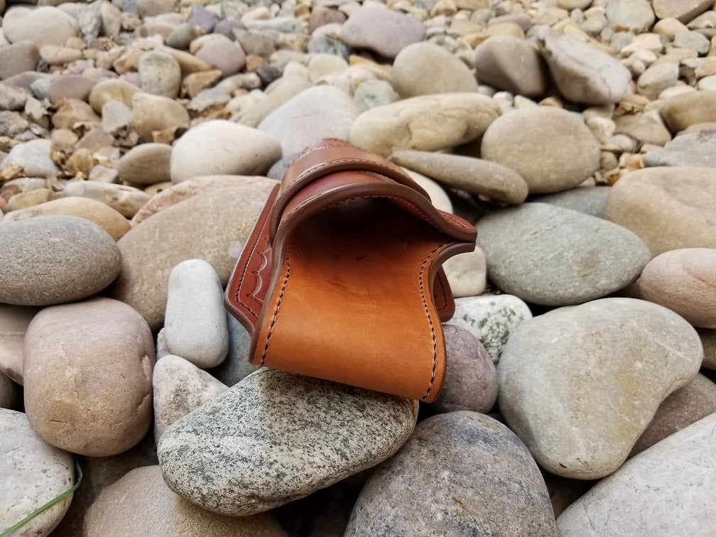 Rear view of the widow rock holster. The piece is a brown leather quickdraw style holster sitting on a bed of pale rocks.