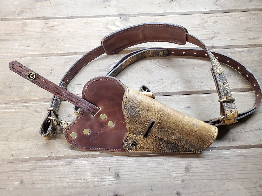 Distressed brown shoulder holster displayed on wooden slats, featuring solid brass hardware and empty holster.