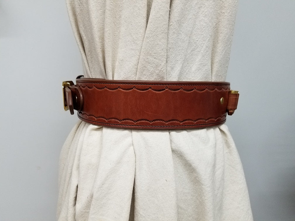 Side view of the widow rock gun rig. The gun rig is made of brown leather, solid brass hardware, and tooled in a scallop pattern along the borders.