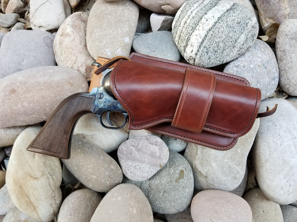 Beautiful brown leather holster containing an old west style revolver sits on river rocks. The holster is clean and simple, with a straight collar and beautiful leather grain.