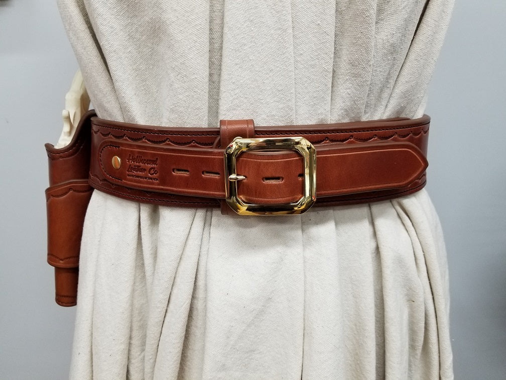 Widow rock gun rig on a white mannequin. The rig is made of brown leather and features brass hardware with a scallop pattern tooled border.
