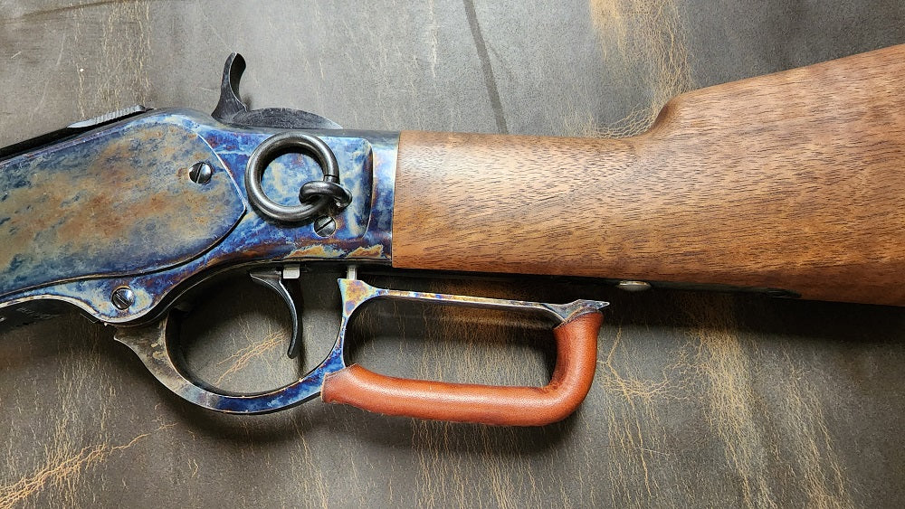 Close up shot of a brown leather wrap on the lever of a winchester lever action rifle, the leather sits on a distressed brown background.